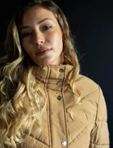 Campera de abrigo negra marca Michael Kors, con cierre central oculto y botones a presión, bolsillos delanteros, puños elastizados, avíos metálicos dorados con logo y capucha de piel sintética desmontable.