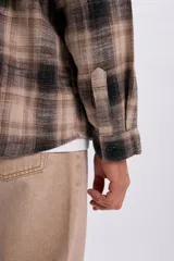 Sobrecamisa de franela a cuadros en tonos tostado y negro, de manga larga, con cierre frontal de botones y un bolsillo aplicado en el pecho.