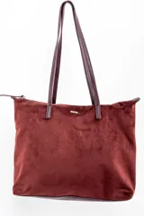 Bolso tipo tote de gran tamaño en color bordó, confeccionado en material sintético con textura de gamuza. Cuenta con cierre superior, correas largas de hombro en tono marrón oscuro y una placa metálica decorativa en el frente.