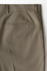 Pantalón de traje slim fit de color marrón topo, con cierre frontal de botón y cremallera oculta, bolsillos laterales y raya central marcada en las piernas.