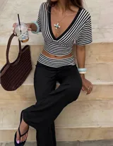 Conjunto compuesto por un top cropped de rayas blancas y negras, con escote en V y mangas cortas, y un pantalón largo negro de pierna ancha con cintura baja y detalle de rayas a juego.