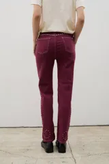 Pantalón de denim negro con diseño de tachas metálicas distribuidas en patrones curvos. Presenta un corte recto y tiro medio.