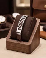 Pulsera compuesta por una banda de acero inoxidable con diseño calado geométrico y una correa de cuerina trenzada en color marrón.
