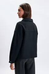 Abrigo corto de paño en color negro, con cuello camisero, cierre frontal con botones metálicos y dos bolsillos delanteros con solapa y botón.