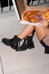 Bota tipo chelsea de cuero negro con suela track y diseño de águila bordado en hilo blanco en la parte frontal.