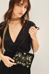 Cartera de mano o bandolera pequeña de terciopelo negro con bordado floral multicolor y apliques de lentejuelas y cuentas brillantes. Correa delgada negra con tachas doradas.