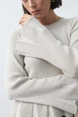 Top de tejido acanalado con sutil acabado metalizado, de silueta entallada con diseño peplum en la cintura y mangas largas levemente acampanadas.