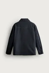 Sobrecamisa regular fit confeccionada en tejido de algodón negro con estructura canvas. Tiene cuello solapa, manga larga con puño abotonado, bolsillos de plastrón con solapa en la cadera y un bolsillo en el pecho. Cierre frontal con botones ocultos bajo solapa.