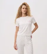 Pijama largo Lov de dos piezas confeccionado en tejido peach touch color blanco con delicado estampado floral y texto frontal, compuesto por remera de manga corta con cuello redondo y pantalón jogger con cintura elastizada.