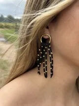 Aros colgantes con base dorada y flecos de cuero sintético negro con cuentas metálicas doradas.