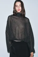 Blusa negra con estampado de lunares blancos, cuello redondo con lazadas y manga larga con puños ajustados. El bajo es ajustable con cordones.