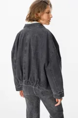 Chaqueta de jean color gris lavado, con corte oversize, mangas amplias y bolsillos frontales con solapa. Presenta cierre frontal con botones metálicos y cuello clásico.
