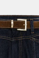 Jeans de mezclilla azul oscuro, tiro medio, corte recto y slim. Presenta costuras verticales marcadas en el frente de ambas piernas y viene con un cinturón de cuero marrón.