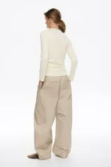 Pantalón de algodón color beige, de corte barrel ancho con tiro bajo. Presenta bolsillos en costuras delanteros y con vivo en la parte trasera. El bajo de la pierna tiene trabillas para ajustar el volumen.