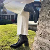Botas cortas de cuero negro, con combinación de texturas de efecto reptil, taco ancho y plataforma delantera. Presentan detalles de tachas metálicas en el lateral y costuras pespuntadas.