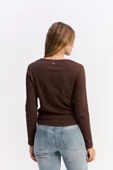 Remera de manga larga color marrón, con cuello redondo y estampa sutil en el pecho con diseño de juego de ta-te-ti y texto.