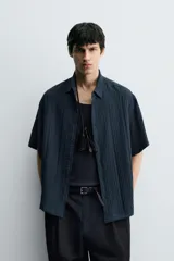 Camisa de corte relajado confeccionada en tejido fluido con textura acanalada. Presenta cuello solapa, manga corta y cierre frontal con botones.