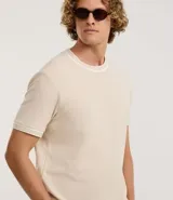 Remera de corte regular confeccionada en tejido texturizado de algodón y poliéster. Presenta cuello redondo y bordes de mangas con detalle de rayas contrastantes en blanco y gris.