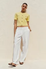 Chaqueta de punto color amarillo pálido, con cuello redondo, manga corta, cierre frontal con botones dorados y bolsillos de parche en el pecho.