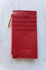 Tarjetero rojo de cuero vacuno con ranuras para tarjetas, cierre con cremallera dorada y bolsillo exterior en la parte posterior.
