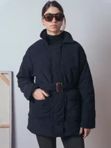 Campera de pana color marrón, con diseño acolchado, cuello camisero, cierre frontal oculto y cinturón ajustable con hebilla a tono. Presenta bolsillos frontales con solapa y mangas largas de corte holgado.