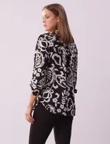 Blusa de gasa estampada con diseño geométrico multicolor, cuello a la base con escote en V y abertura frontal con botones. Presenta detalle de plisado en la parte delantera y mangas largas con sistema de ajuste mediante presilla y botón.