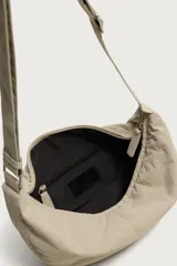 Bolso de hombro de nylon color negro, con diseño curvo y cierre de cremallera en el compartimento principal. Cuenta con asa ajustable para llevar al hombro y bolsillo interior con cierre.