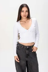 Remera manga larga blanca de tejido acanalado, con profundo escote en V cruzado decorado con tachas metálicas en los bordes.