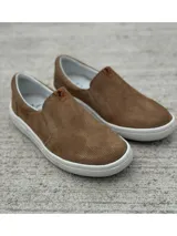 Zapato slip-on verde oscuro de gamuza con perforaciones, suela blanca y elástico lateral.