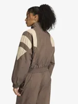Campera deportiva Adidas de corte oversize, con cierre frontal completo y cuello alto. Presenta un diseño de bloques de color en tonos marrón y beige, inspirado en el estilo Equipment de los años 90, con puños y cintura elásticos.