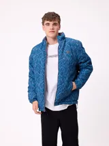 Campera reversible de nylon con cuello alto y cierre frontal. Un lado es de color gris liso con logo bordado, mientras que el otro lado presenta un estampado abstracto en tonos azules. Cuenta con bolsillos laterales y puños elásticos.