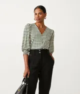 Blusa de jersey con estampado geométrico en tonos blanco, negro y verde. Tiene escote en V, mangas 3/4 abullonadas con elástico en los puños y cierre frontal con botones.