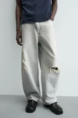 Jeans de mezclilla, tiro medio, color celeste claro lavado con efecto desgastado y roturas pronunciadas en ambas piernas. Corte ancho y relajado.