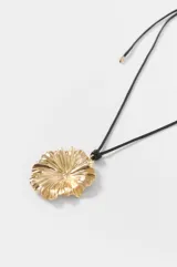 Collar largo con cordón negro y dije colgante metálico dorado con forma de flor o concha marina texturizada.