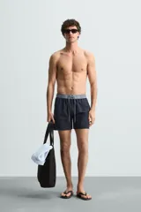 Bañador de hombre azul marino con cintura elástica gris y cordón ajustable. Presenta un pequeño texto estampado en relieve en la parte inferior izquierda.