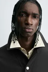 Sobrecamisa negra de algodón con estructura canvas, corte cropped y calce holgado. Presenta cuello solapa, manga larga, bolsillos laterales en cadera y cierre frontal con botones a presión metálicos.