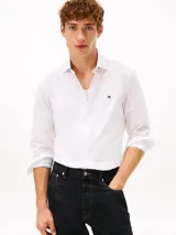 Camisa de vestir Tommy Hilfiger de color blanco, corte slim y manga larga. Presenta cuello camisero, cierre frontal con botones, puños abotonados con vuelta estampada en el interior y el logo de la marca bordado en el pecho.