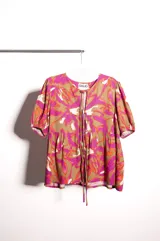 Blusa de lino bordado con estampado floral en tonos fucsia, marrón y blanco, de calce holgado, escote en V con cordones para atar y mangas cortas abullonadas.