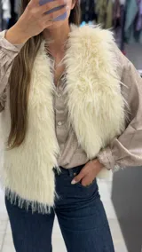 Chaleco de piel sintética en color natural, con diseño sin mangas y frente abierto. Presenta una textura de pelo largo y suave, ideal para complementar looks de invierno.