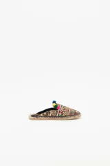 Zueco de punta cerrada con diseño multicolor, decorado con bordados étnicos, lentejuelas, canutillos y pompones de colores. Presenta una suela de yute tipo alpargata con un pequeño taco de madera de 1,5 cm y forro de cuero caprino.