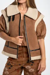 Chaleco estilo gamulán de color negro, con interior y cuello de corderito sintético. Presenta cierre frontal, detalles en cuero sintético y corte oversize.