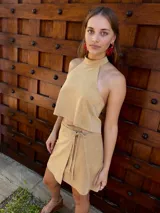 Falda corta tipo pareo confeccionada en cuero beige, con diseño envolvente que se ajusta mediante tiritas de cuero en la cintura.