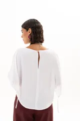 Blusa blanca de corte holgado y diseño minimalista, con mangas cortas tipo murciélago que presentan un detalle de fruncido lateral con cordón ajustable.