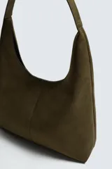 Bolso de hombro liso color verde militar, con compartimento principal con cierre de imán y un bolsillo interior con cremallera. Tiene un asa de hombro.