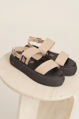 Sandalias de plataforma con suela negra y tiras en color beige. Cuentan con cierre de hebilla ajustable en el tobillo y detalle de etiqueta de marca en el lateral.