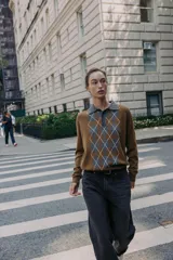 Jersey de punto con cuello polo y cierre frontal de botones. Presenta un diseño de estampado de rombos en el frente en tonos gris y blanco sobre una base color marrón.