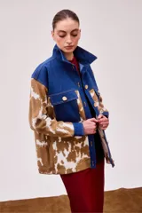 Chaqueta con corte camisero, cuello y solapa de jeans color índigo. Tejido que llega bajo la cadera con bolsillos laterales. Pattern de vaca en tonos café y crudo en las mangas y parte inferior.