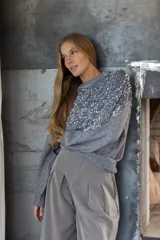 Buzo de punto color gris con diseño holgado, cuello redondo y detalle de lentejuelas plateadas en la parte frontal superior y hombros.