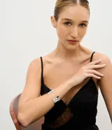 Pulsera rígida de metal plateado con diseño abierto y detalle de perla aplicada en los extremos.