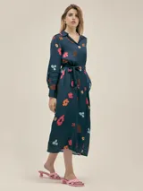 Vestido largo camisero azul marino con estampado de flores de colores, confeccionado en seda viscosa. Tiene cuello camisero, cierre frontal con botones nacarados, lazo para ajustar en la cintura, bolsillos laterales y aberturas laterales en el ruedo.